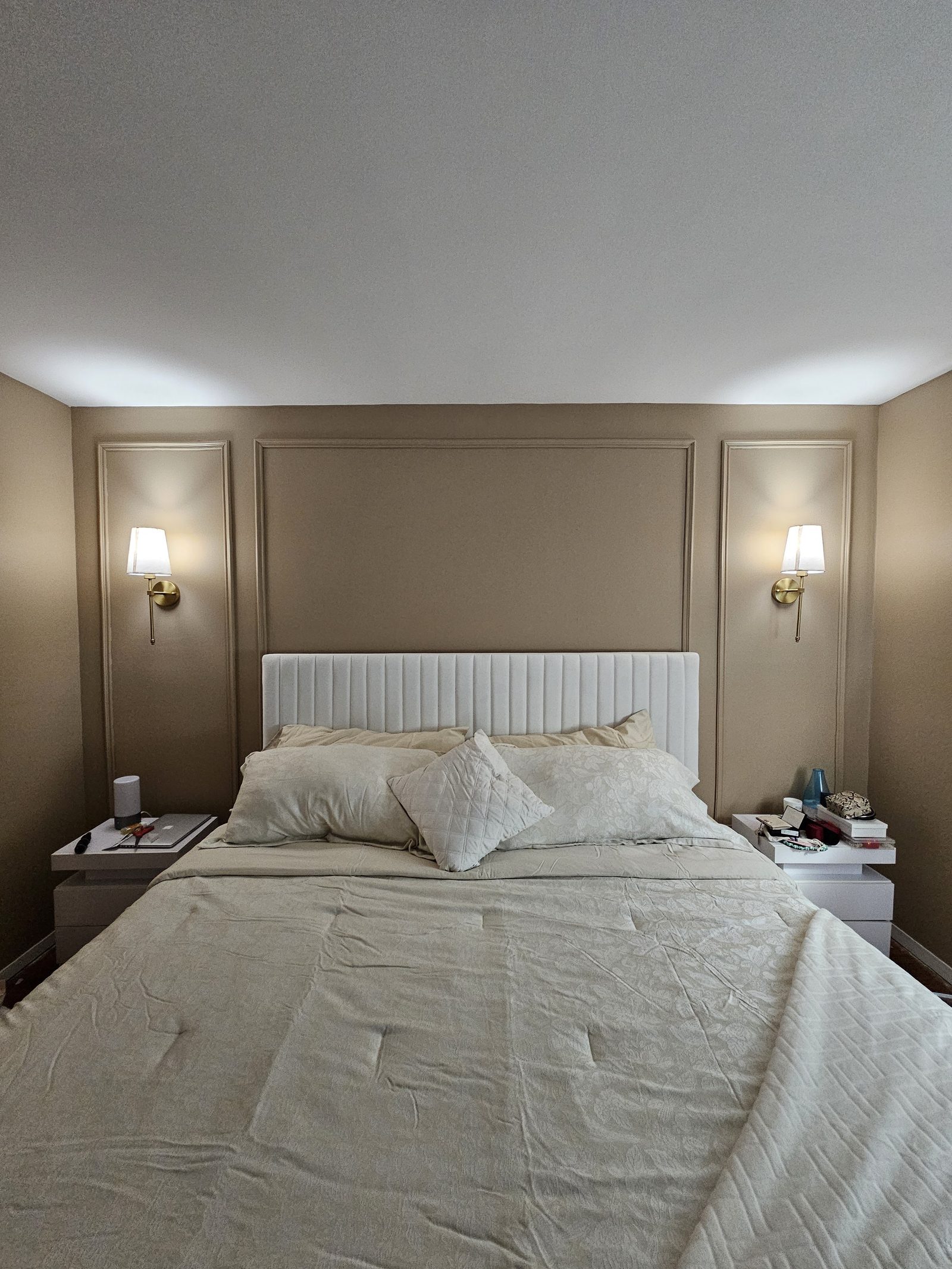 Primary suite remodel with upholstered channel headboard, wall paneling, and brass sconces
